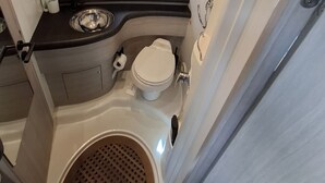 Een kleine badkamer in een camper, met toilet, wastafel en douchehoek.