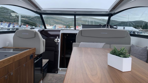 A boat interior with a dining area, two seats, a small kitchen, and a view of the marina. - Sun-kissed Sailing Adventure in Split-Dalmatia, Croatia (Trogir)
