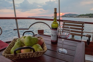 A wooden table with a wicker basket of fruit, a bottle of wine, and a wine glass on a boat deck. - Sun-Kissed Sailing Adventure in Split, Croatia (Split)