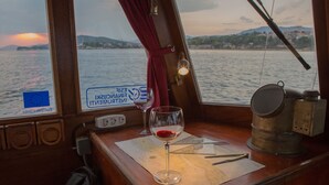 Ein Holztisch mit einer Seekarte, einem Weinglas und einem Metallbehälter auf einem Schiffsdeck.