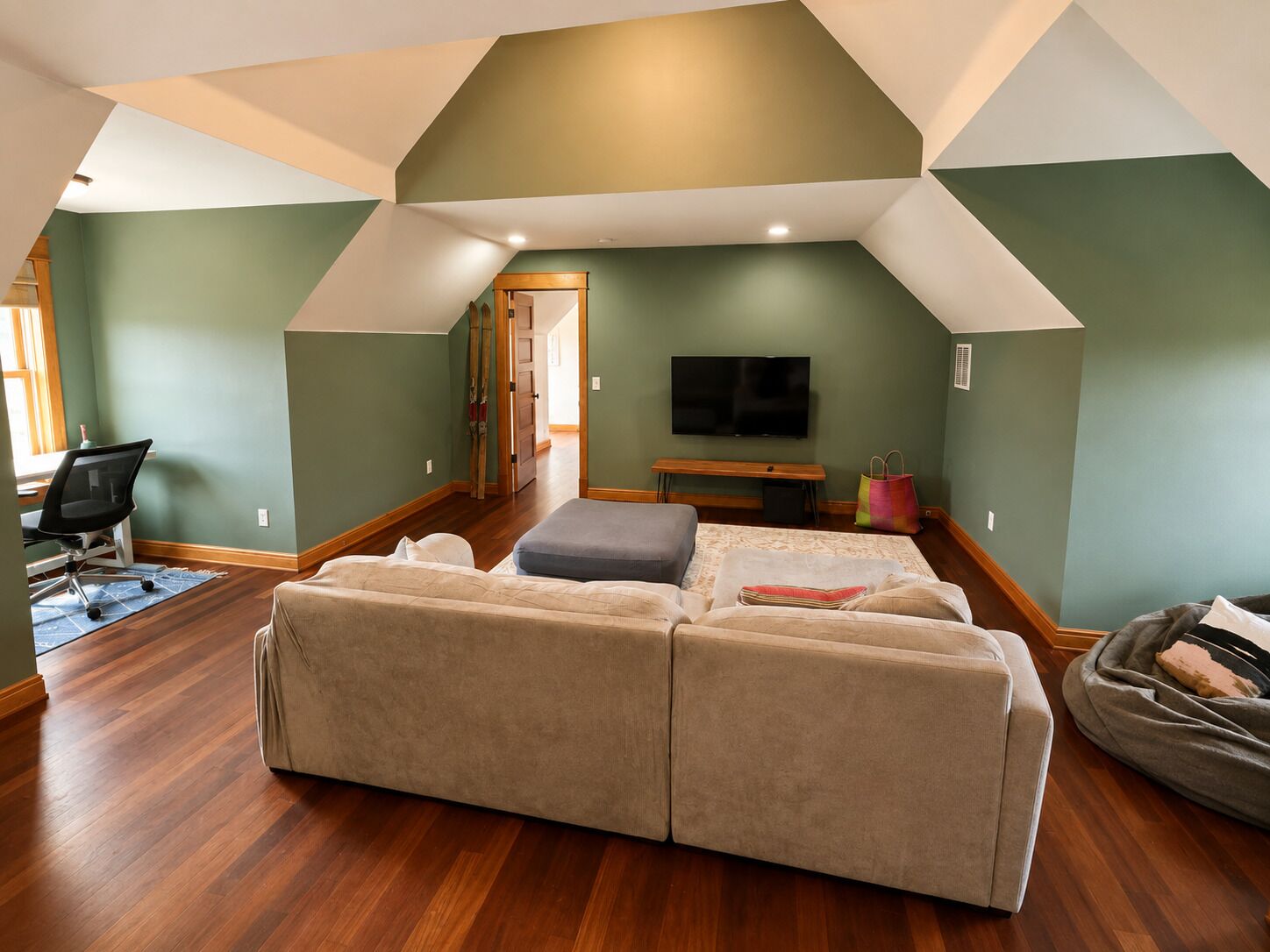 A loft-style room with a large sectional sofa, a flat-screen TV, and a wooden floor.