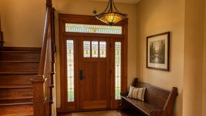 A wooden staircase leading to a door with stained glass panels, a bench with a cushion, and a framed picture on the wall.