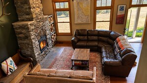 A cozy living room with a stone fireplace, leather sofas, and a large window.