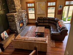 Una sala de estar acogedora con chimenea de piedra, sofás de cuero y un ventanal grande.