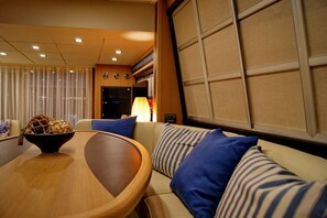 Ein Zimmer mit einem runden Holztisch, einer Couch mit gestreiften Kissen und einem großen Fenster mit Jalousien.