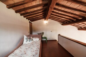Une chambre avec un plafond en pente, un lit avec une literie à motifs floraux, une table de chevet et un radiateur fixé au mur.