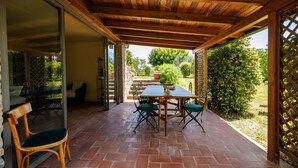 Un patio exterior con una mesa y sillas de madera, un vidrio que da a un área de patio, y vistas de un jardín.