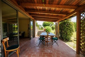 An outdoor patio with a wooden table and chairs, a glass door leading to a patio area, and a view of a garden. - A spacious 120 sqm apartment, ideal for six guests, situated within a charming estate in the Chianti hills in a peaceful setting along a traffic-free road. Guests have access to a private garden with a furnished patio - perfect for enjoying the outdoors  (Castelnuovo Berardenga)