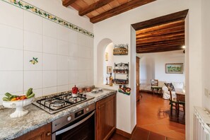 A kitchen with white tiles, a gas stove, and a dining area with a table and chairs. - A spacious 120 sqm apartment, ideal for six guests, situated within a charming estate in the Chianti hills in a peaceful setting along a traffic-free road. Guests have access to a private garden with a furnished patio - perfect for enjoying the outdoors  (Castelnuovo Berardenga)