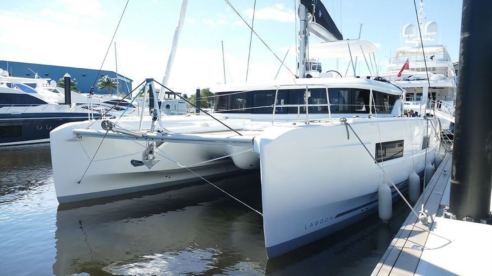A white yacht docked at a marina with other boats in the background.