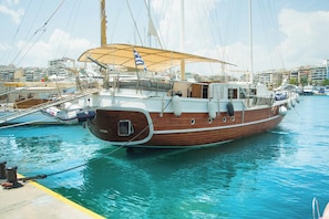 A large wooden boat docked at a marina with a covered deck and a flag.