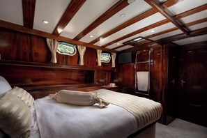 A cabin with a bed, wooden paneling, a TV, and a window.