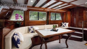Eine Holzhütte mit bequemen Sitzbänken, einem Tisch und Fenstern mit Blick auf viel Grün.