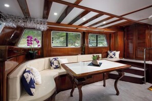 A cabin with a wooden interior, a cushioned bench, a table, and windows with views of greenery. - Sun-Kissed Sailing Adventure in Split, Croatia (Split)