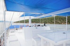 A boat deck with a covered seating area, lifebuoys, and a steering wheel.