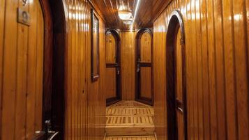 A wooden interior hallway with doors marked with numbers, a central staircase, and a ceiling light fixture.