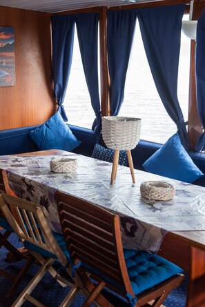 A dining area with a table set for two, blue upholstered seating, and a view of the sea through large windows.
