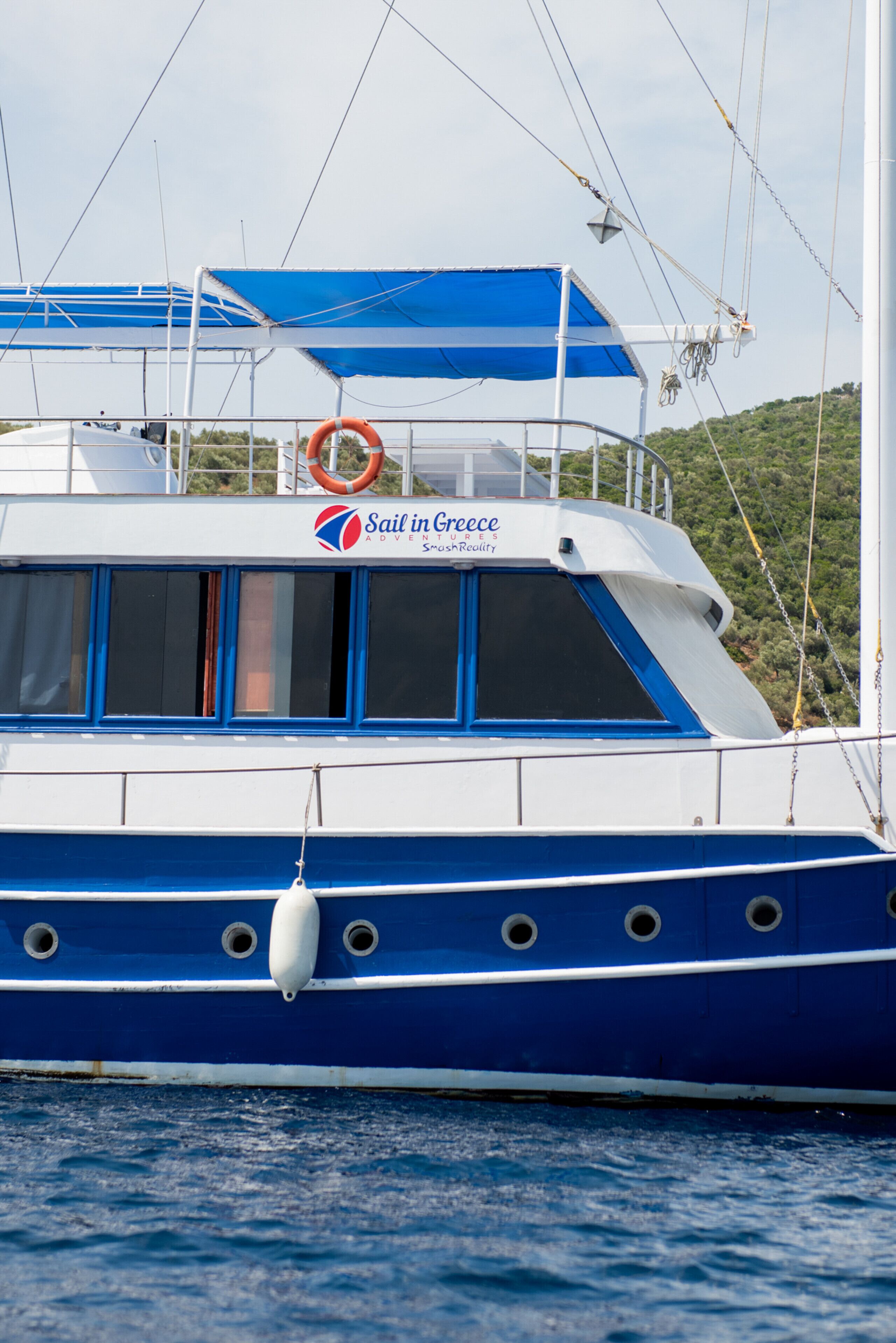 Ein Boot mit blau-weißer Gestaltung, einem Schriftzug 'Sail in Greece' und einem Rettungsring.