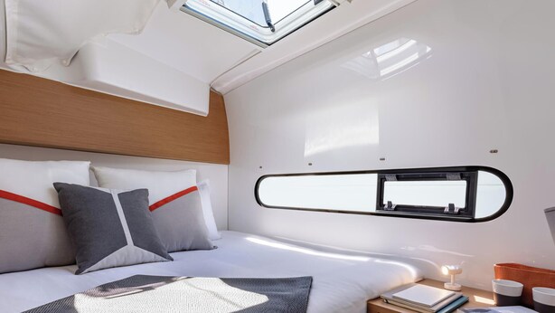 Een moderne slaapkamer met dakraam, een bed met kussens, een nachtkastje met lamp en een spiegel.