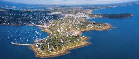 Vue aérienne d’une ville côtière avec un port de plaisance, des zones résidentielles et un phare.