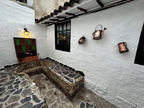 Ein Innenhof mit Steinpflasterung, einer Holztür mit grünen Glasfeldern und zwei Fenstern mit schwarzen Rahmen.