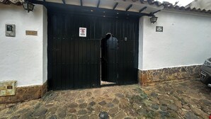 Une entrée fermée par un portail, agrémentée d’un panneau indiquant « Stationnement interdit », une allée pavée de pierres et un véhicule garé sur le côté droit.