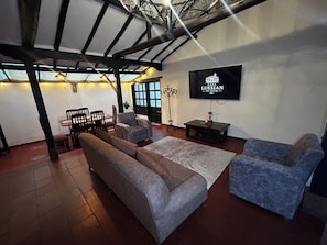 A living room with a sofa, armchairs, a TV, and a dining area with chairs and a table.