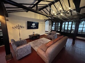 Ein Wohnzimmer mit Sofa, zwei Sesseln, einem Fernseher, einer Chandelier und Blick durch große Fenster.