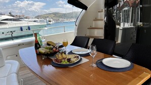 En matplats på en lyxyacht med ett bord dukat för två personer, utsikt över hamnen och en båt i bakgrunden.