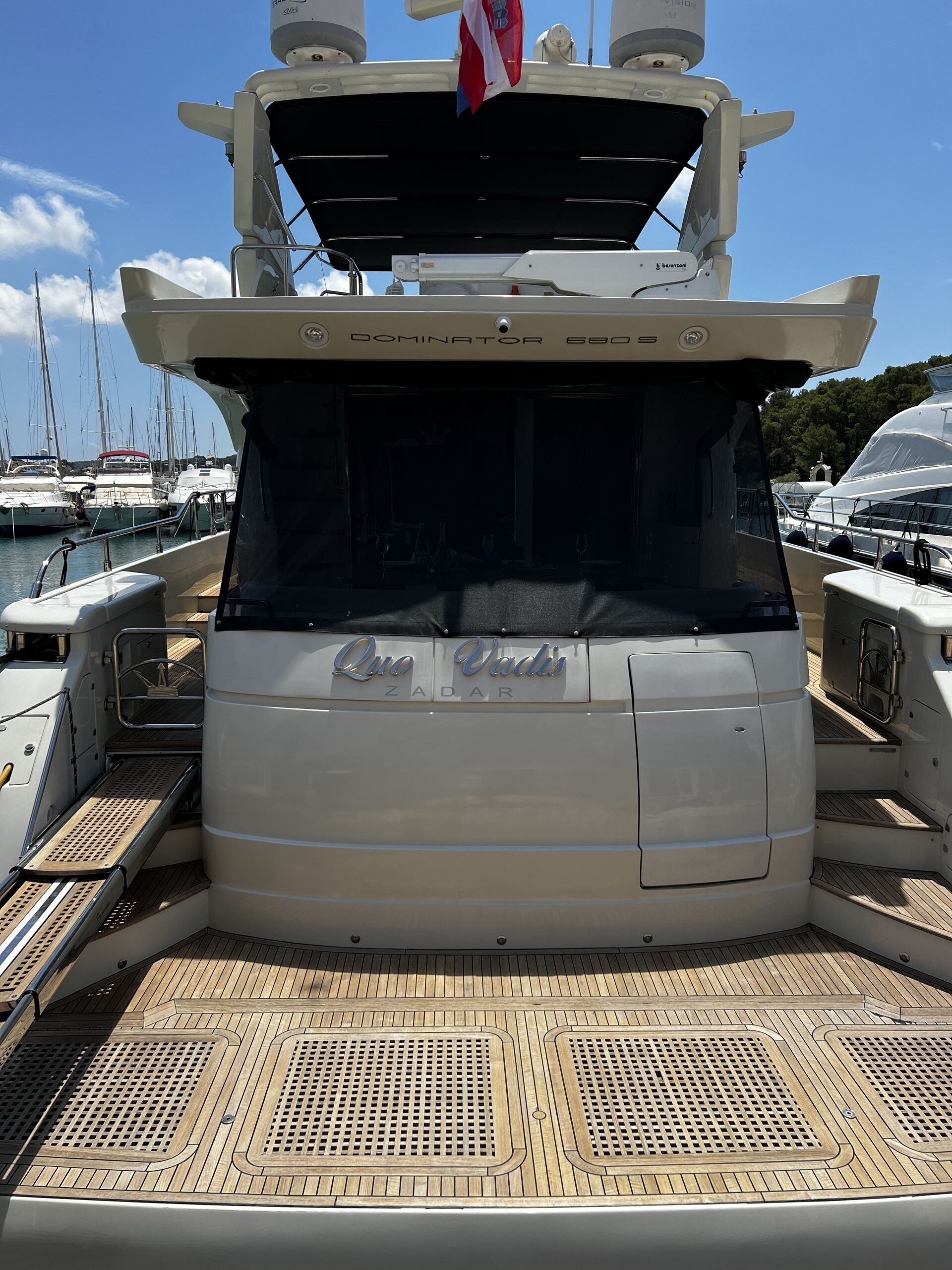 A yacht named 'Quo Vadis' docked at a marina with a clear sky.