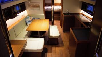 A compact interior with a sofa, a table, a bench, a bunk bed, and a small kitchenette.