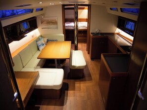 A compact interior with a sofa, a table, a bench, a bunk bed, and a small kitchenette.