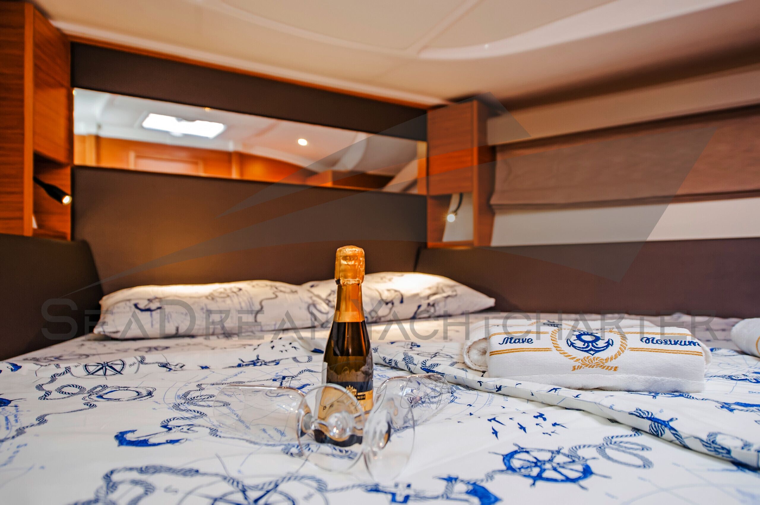 A bed with a bottle of champagne, glasses, and a towel with a nautical design.