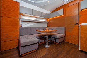 A compact, modern interior with a wooden floor, a cushioned seating area, a small table, and built-in cabinets. - Sun-Kissed Sailing Adventure in Zadar, Croatia (Bibinje)