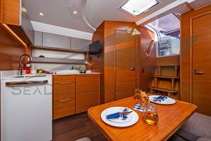 A compact kitchen with a dining area, wooden cabinetry, a built-in TV, and a small window. - Sun-Kissed Sailing Adventure in Zadar, Croatia (Bibinje)