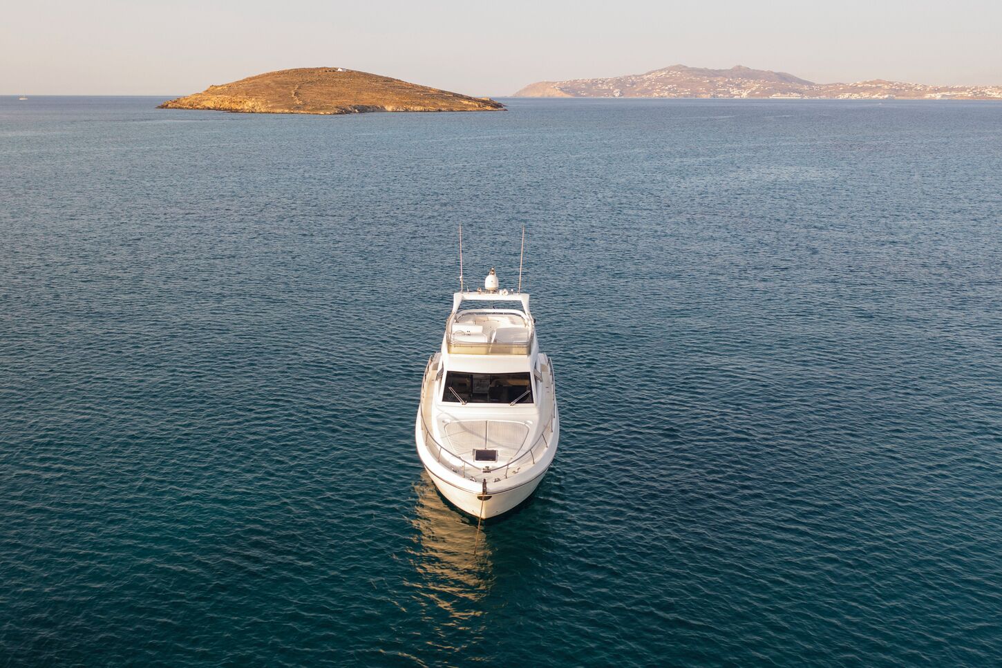 Uno yacht ancorato in acque calme con un'isola e montagne sullo sfondo.