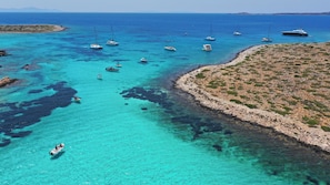 Eine Küstenlandschaft mit Booten, klarem türkisblauem Wasser, felsigem Gelände und einer kleinen Insel.