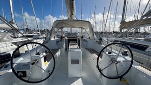 Het dek van een boot met twee stuurwielen, een centrale console en uitzicht op andere boten in de jachthaven.