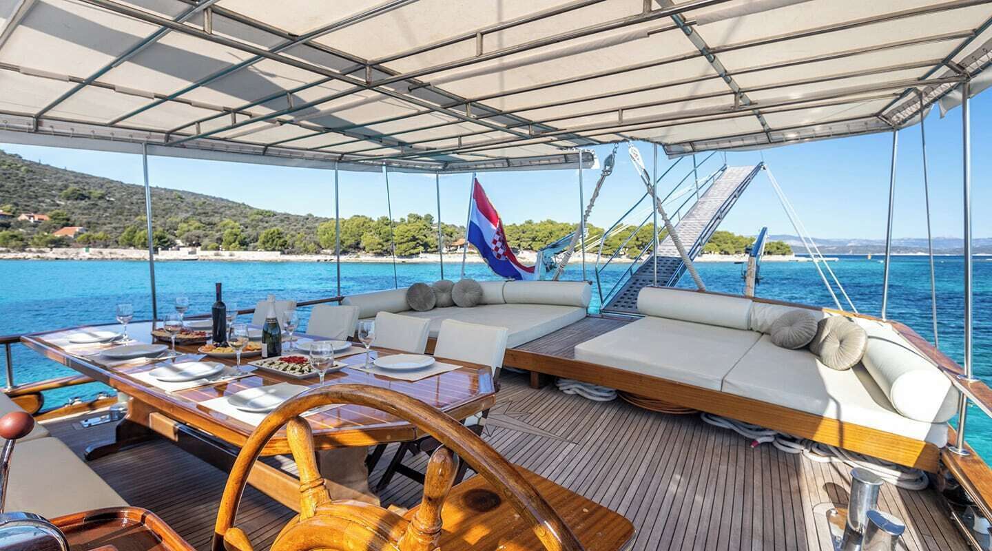 A yacht deck with a dining area, a sofa, and a flag.