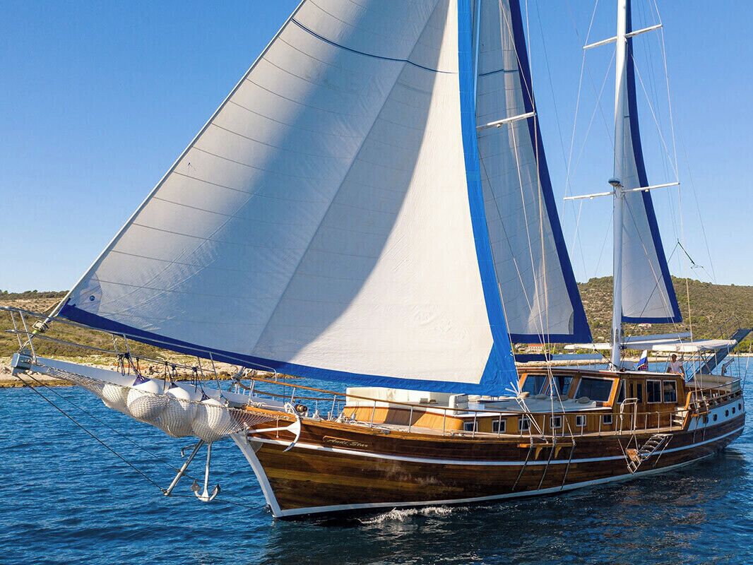 A wooden sailing boat with multiple sails, a cabin, and a deck with seating.