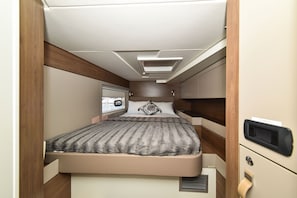 Ein kompaktes Schlafzimmer in einem Wohnmobil mit Bett, Fenster und integriertem Fernseher.