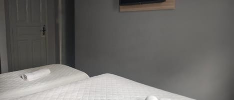 Habitación de hotel con dos camas, un televisor montado en la pared y una puerta.