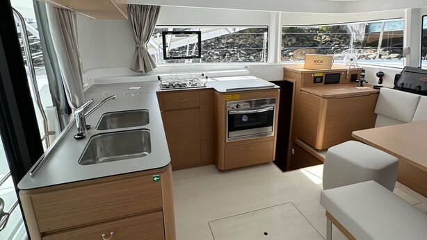 A compact galley with a sink, oven, and storage cabinets, a small seating area, and large windows offering views of the outside. - Sun-Kissed Sailing Adventure in Sibenik, Croatia (Rogoznica)