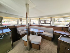Un intérieur de bateau compact comprenant un coin cuisine, un espace salon et des fenêtres donnant sur le port de plaisance.