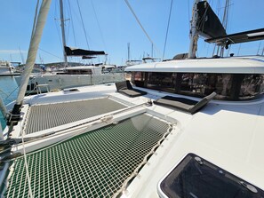 Un pont de bateau doté d’un espace salon couvert, d’une zone délimitée par un filet et offrant une vue sur les autres bateaux amarrés dans la marina.