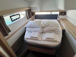 A compact bed with pillows and folded towels, a window with curtains, and a small table. - Sun-Kissed Sailing Adventure in Zadar, Croatia (Bibinje)