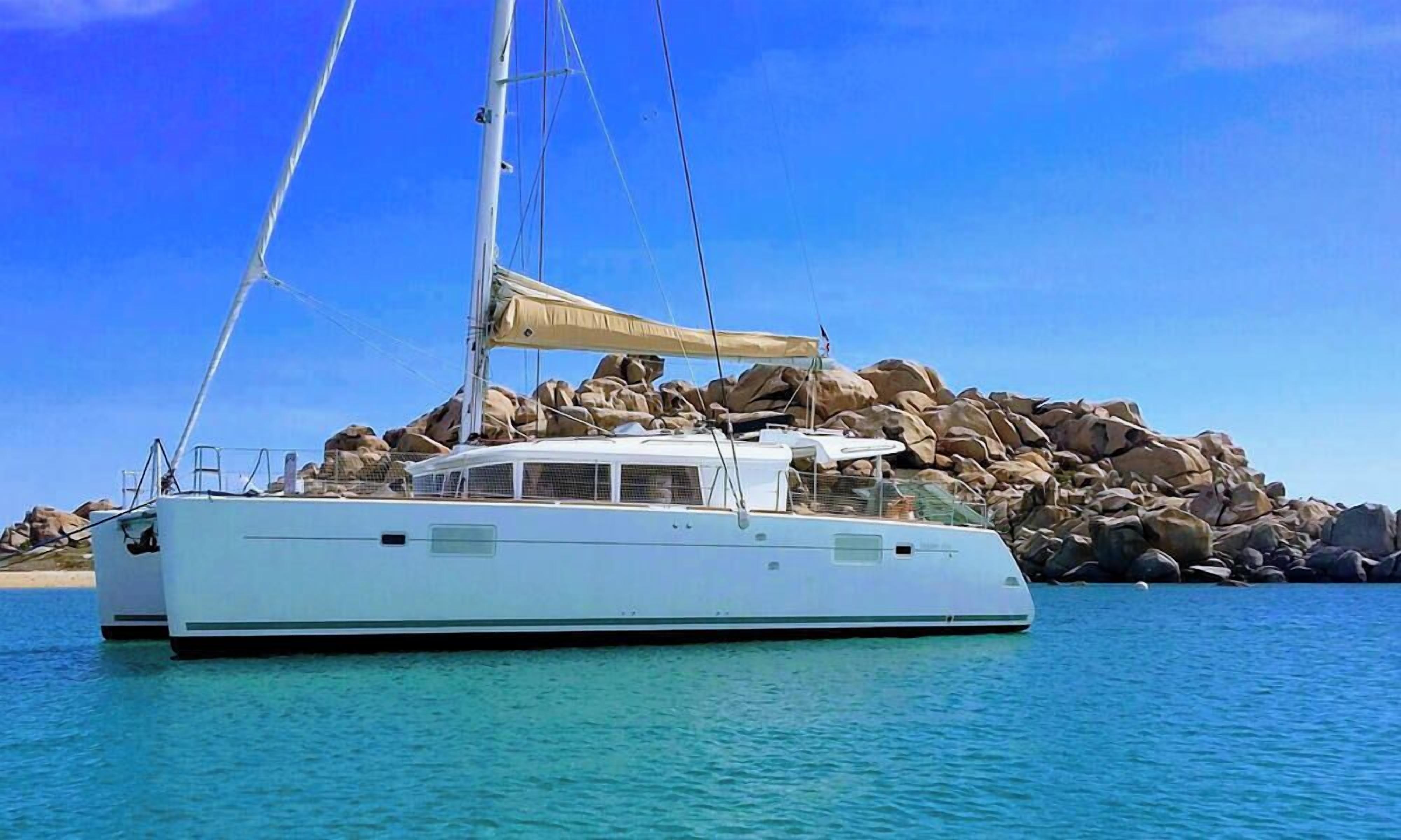 Un yate blanco amarrado cerca de una costa rocosa con agua azul cristalina.
