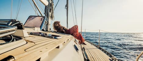 A sailboat deck with a person lying on the edge, a laptop, and ropes.
