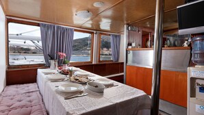 A dining area with a table set for four, a water dispenser, and a view of a bridge and water body. - Sun-Kissed Sailing Adventure in Split-Dalmacia, Croatia (Omiš)