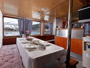 A dining area with a table set for four, a water dispenser, and a view of a bridge and water body. - Sun-Kissed Sailing Adventure in Split-Dalmacia, Croatia (Omiš)